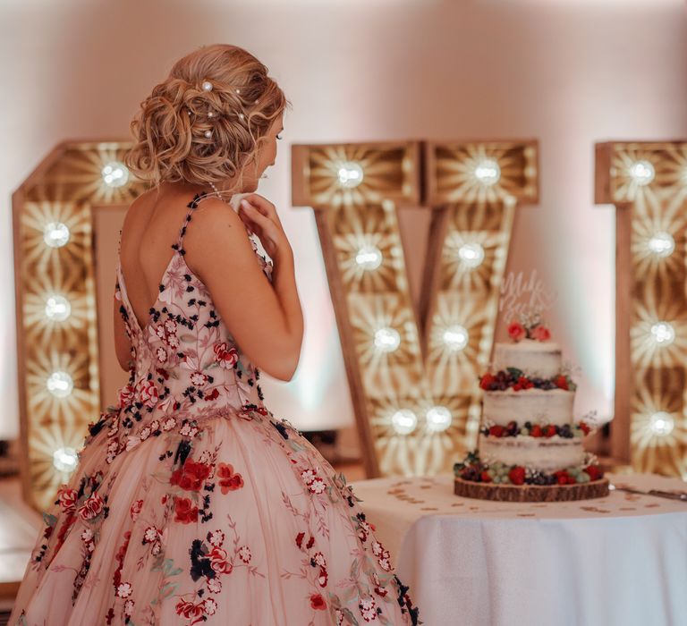 Bride stands in front of LOVE wedding sign with lights 