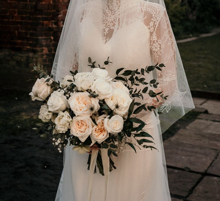 Classic bride in a long sleeve lace wedding dress with sheer veil holding an all rose wedding bouquet 