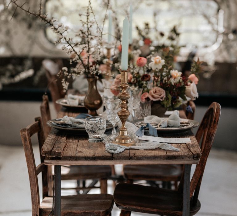 Wooden rustic table with brass candleholders and pastel florals and pale blue napkins