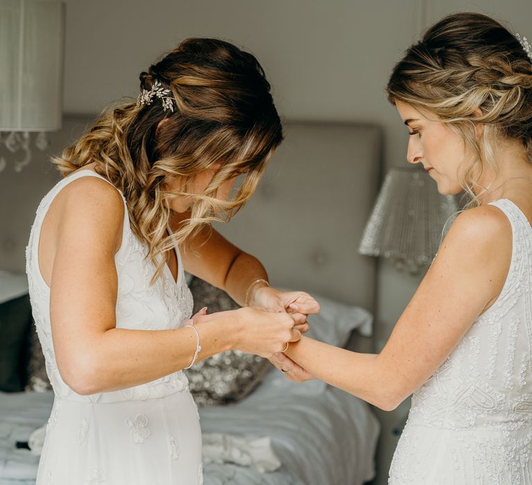 Bride helps wife place bracelet on her wrist on her wedding day