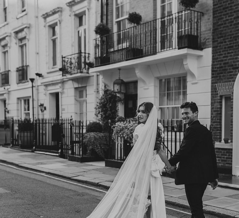 Black and white portrait of a bride in a short wedding dress with her long wedding veil billowing in the wind 