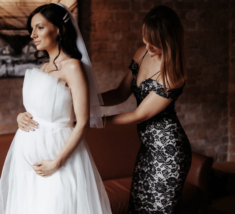 Bride cradles her pregnant tummy as she wears wedding gown with layered tulle skirt