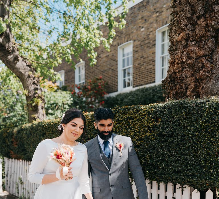 Indian bride & groom walk through Chelsea whilst bride holds small dried floral bouquet