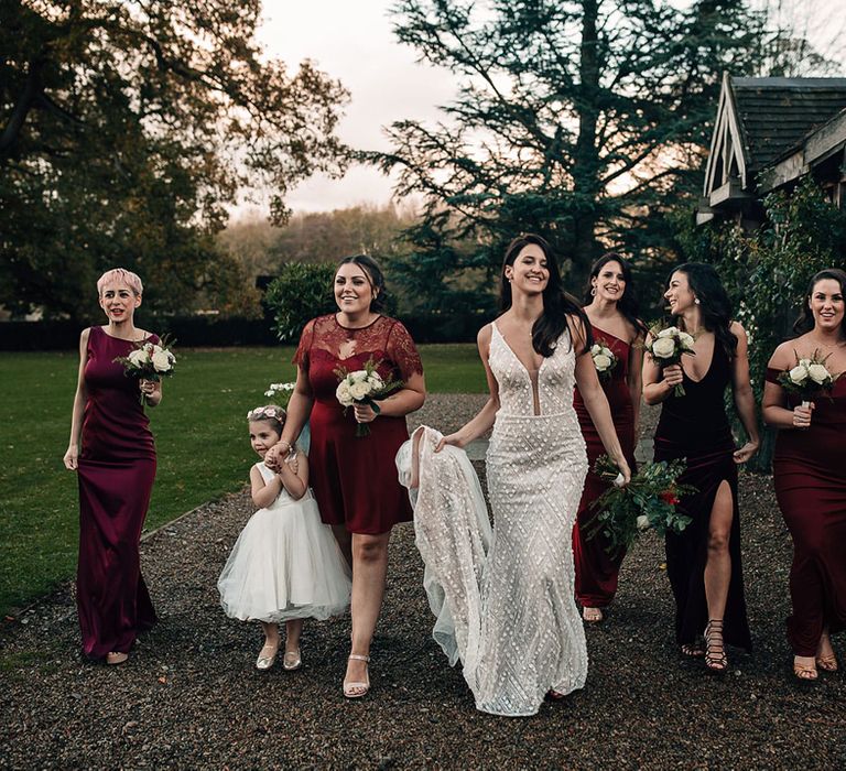 Winter wedding with bride in an embellished wedding dress walking through the venue with her bridesmaids in different style burgundy bridesmaid dresses