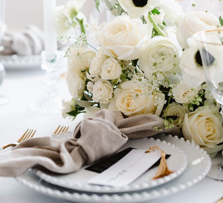 A black centred anemone stands proud within a white wedding bouquet filled with cluster roses, roses, and ranunculus.