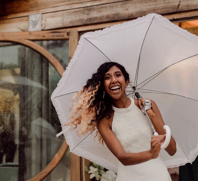 Bride holds white umbrella and wears white reception gown | Joshua Gooding Photography