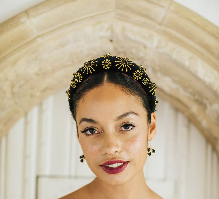 Black bride with swept back hair wearing a gold headband and deep red lipstick