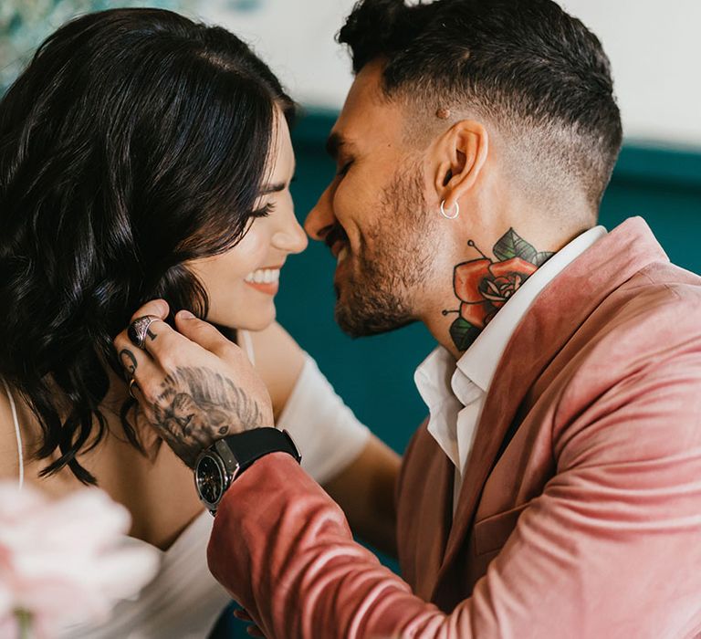 Groom in a pink velvet jacket kissing his bride with short curly hair at their city wedding 