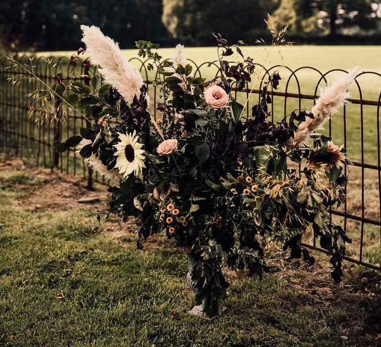 Floral installation in garden with foliage, roses, pampas grass and sunflowers for garden wedding reception in Cornwall