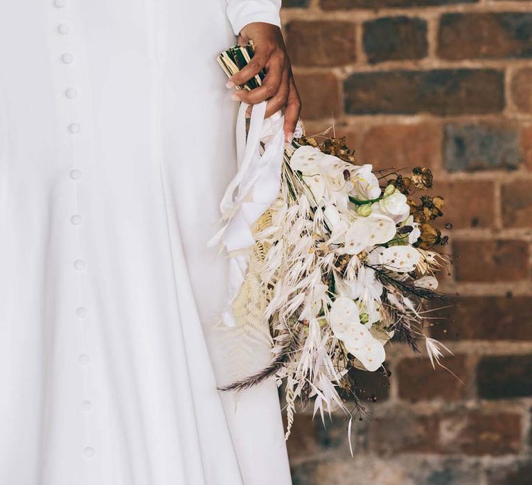 Bride in a sheer long sleeve wedding dress with buttons down the back holding a dried and fresh flower wedding bouquet 