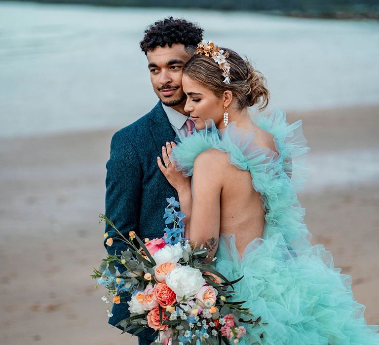 Bride in a mint green tulle wedding dress embracing her husband in a blue wool suit at their pastel beach elopement 