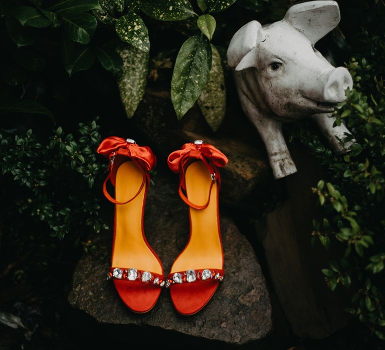 Red heeled sandals with gem encrusted straps and bows placed on rock for The Wellbeing Farm wedding in Lancashire