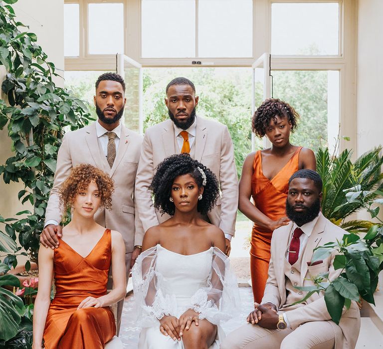 Stylish wedding party in orange satin bridesmaid dresses, beige suits and a strapless wedding dress with side slit