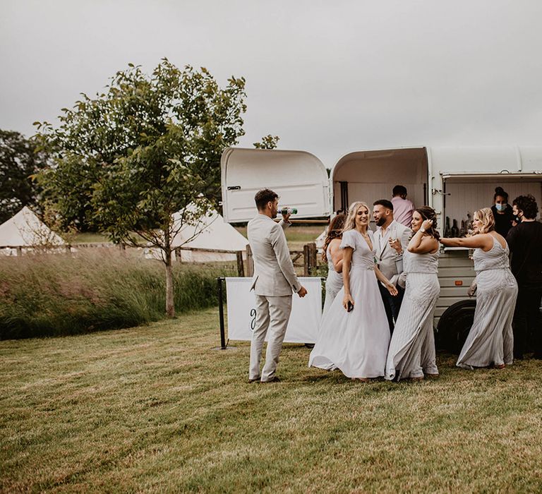 Wedding guests stand outside of cocktail van on wedding day outdoors in field