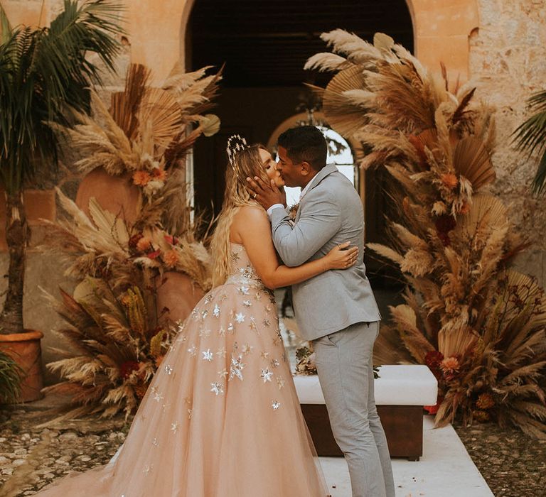 Bride & groom kiss on their wedding day in front of pampas grass installations for wedding in Mallorca 