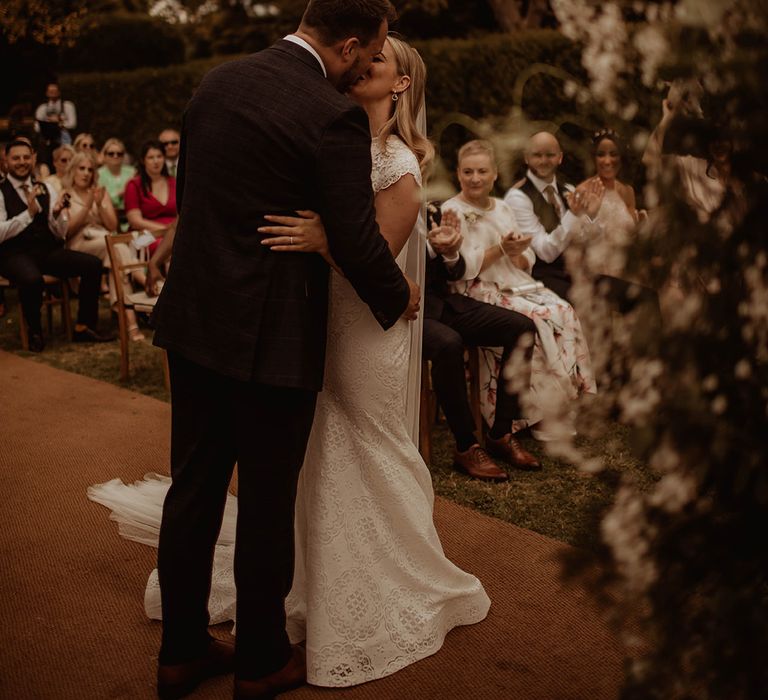 Groom kissing his bride in a lace wedding dress at their outdoor Dewsall Court wedding 