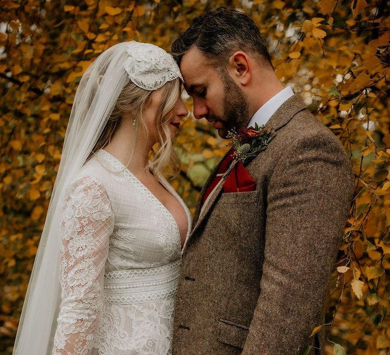 Bride and groom autumn wedding photograph with bride in a lace wedding dress with long sleeves and groom in a tweed suit 