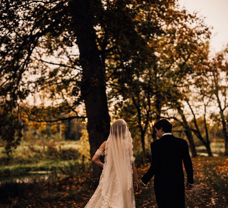 Lace detail dress for bride as she walks through Oxnead Hall grounds with groom