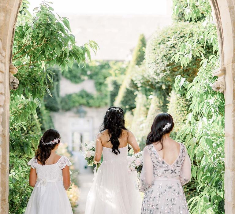 Bride walks with flower girl and bridesmaid wearing embellished gown 