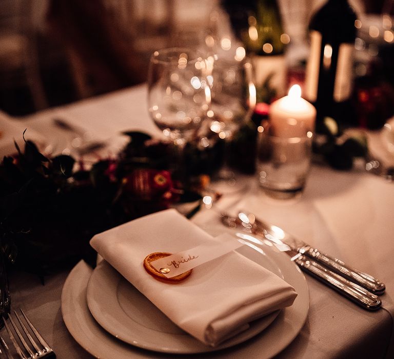 Table mat placing with white napkin, pillar candles & dried oranges on name cards 