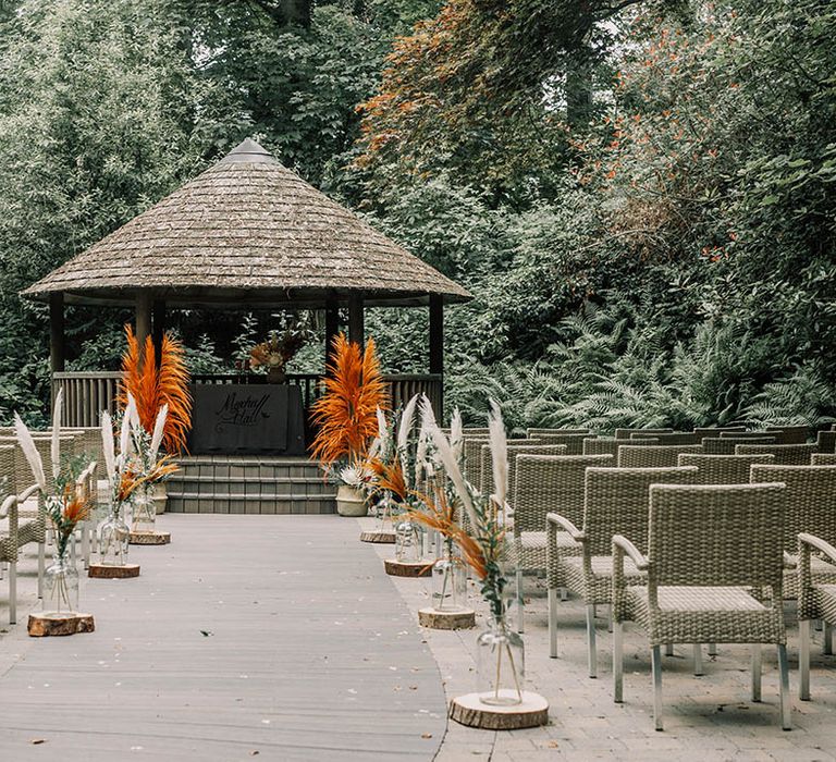 outdoor wedding ceremony complete with bright orange pampas grass toward the end and wicker chairs 