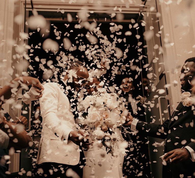 Confetti moment with groom in a white tuxedo jacket and bride in a fitted wedding dress with white wedding bouquet 