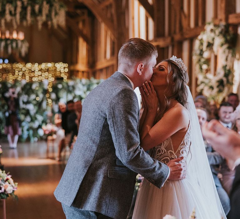 Bride and groom share their first kiss as a married couple in front of wedding guests in rustic wedding venue