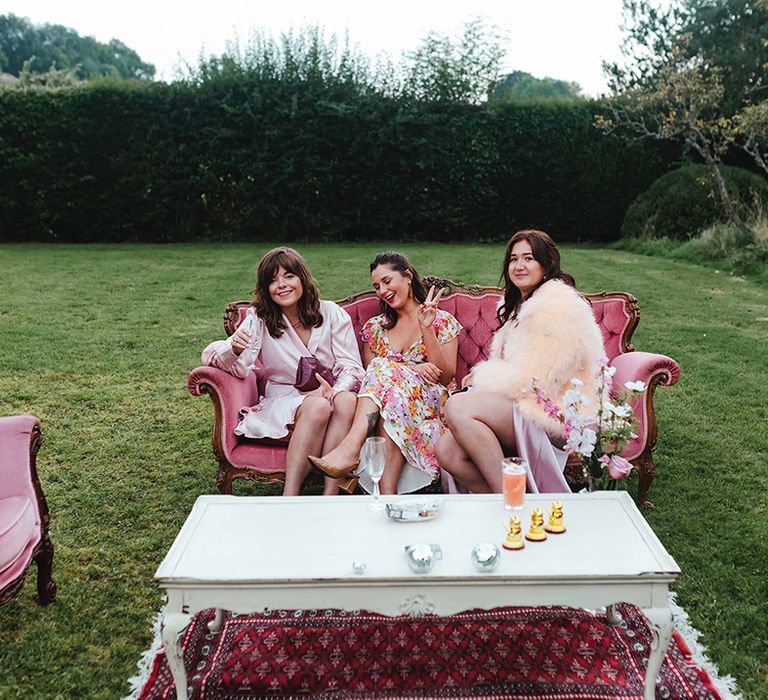 Wedding guests in various shades of pink sit together on pink sofas at outdoor area info summer wedding