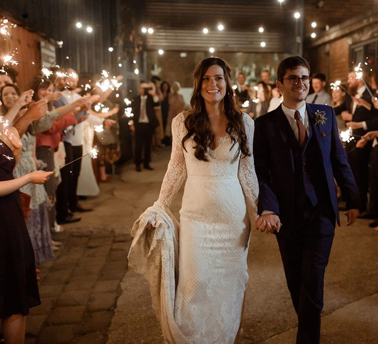 Bride in Maggie Sottero wedding dress and groom in blue suit have a sparkler send off after their church wedding 