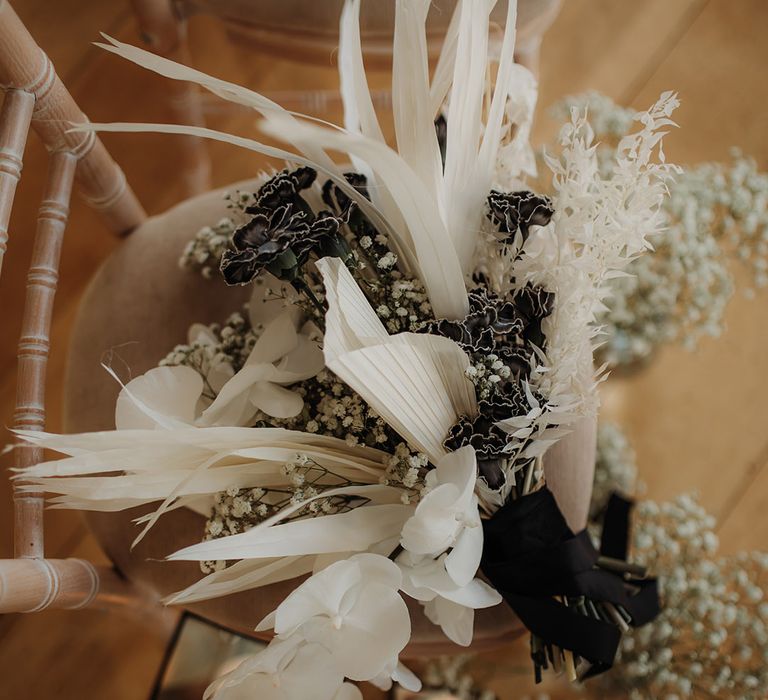 white grasses, orchids and palm leaves wedding bouquet tied with black ribbon