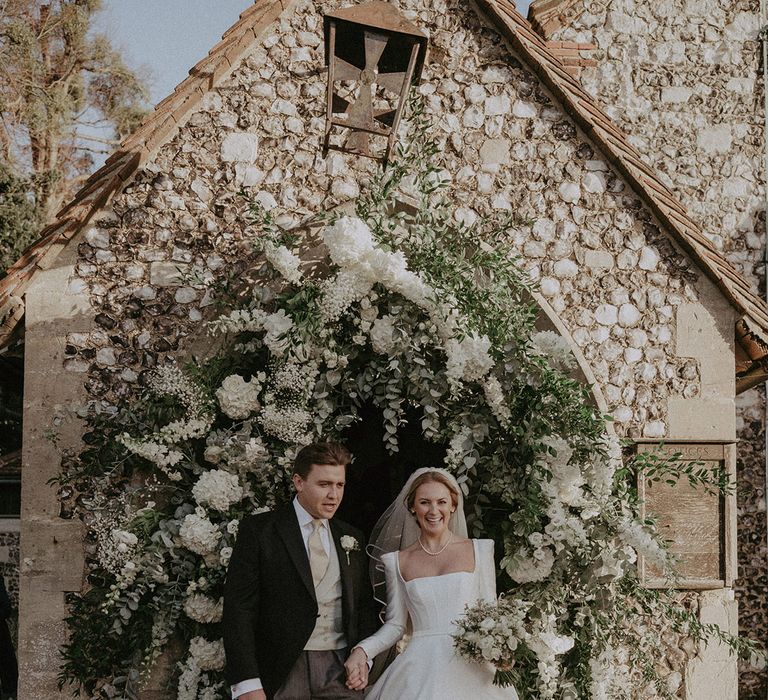 Bride and groom under large white mixed floral arch at Hedsor House wedding