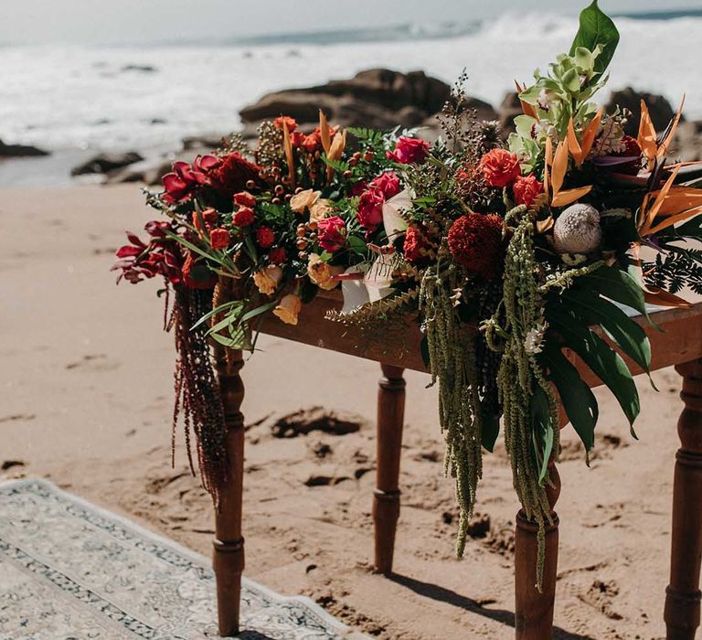 Red and orange flowers with lots of greenery for beach destination wedding