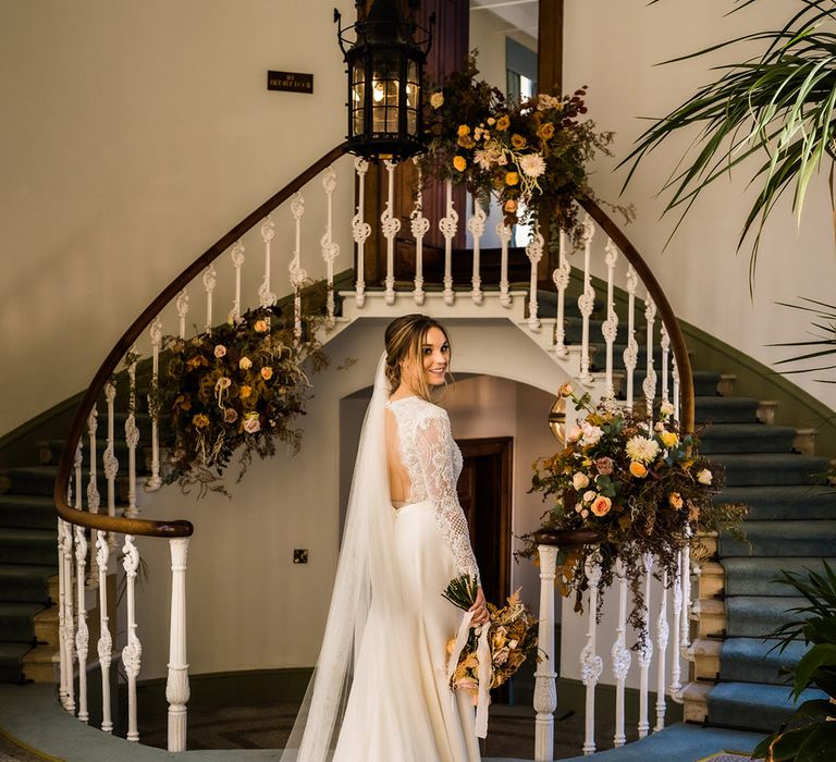 Bride in open back wedding dress with veil and train with lace top and long sleeves with autumnal wedding flowers and bouquet