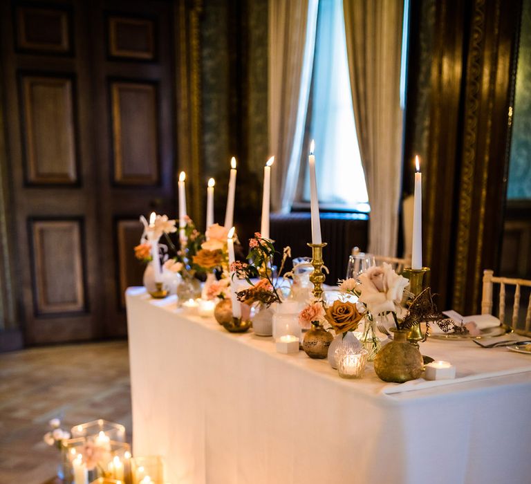 Sweetheart top table for the bride and groom with pillar candles in gold rimmed vases on the floor and tapered candles on table in gold holders