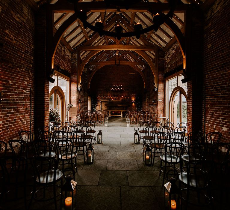 Cosy ceremony room at Hazel Gap Barn with exposed beams, candlelight, fairy lights, dark wood and large lanterns