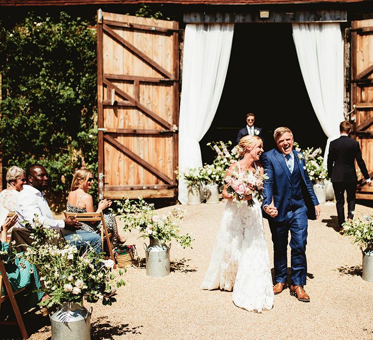 Laughing couple exit their wedding ceremony together on sunny day 