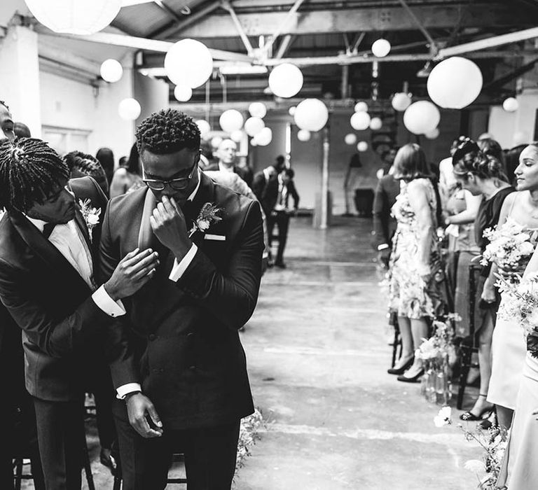 Groomsmen checks on the groom as he starts to get emotional for wedding at industrial wedding venue with hanging white paper lanterns