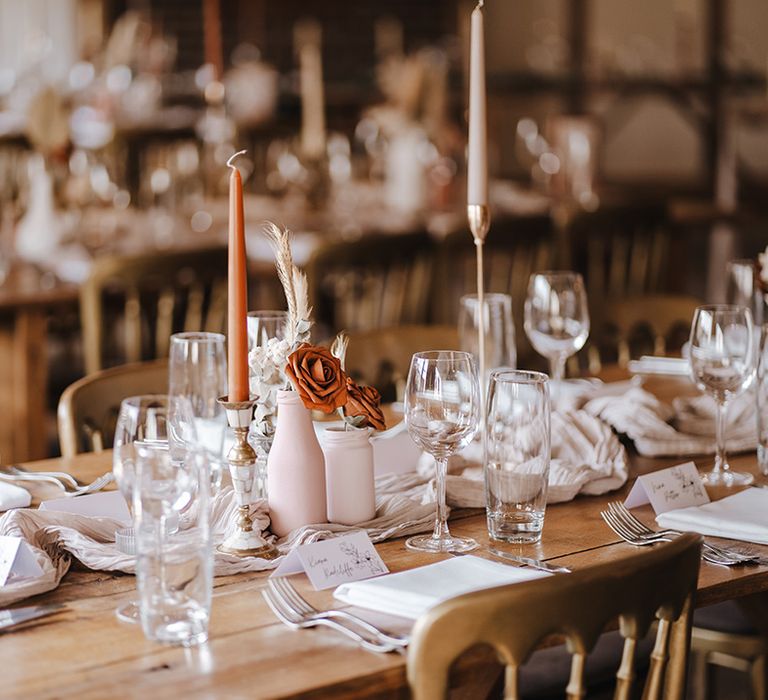 Boho luxe wedding table setting with orange, rust, pink tapered candles with neutral flowers and linen tablecloth