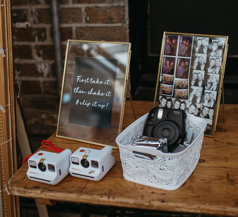 Polaroid cameras with basket of film for wedding guests to take pictures of themselves with gold photo frame sign