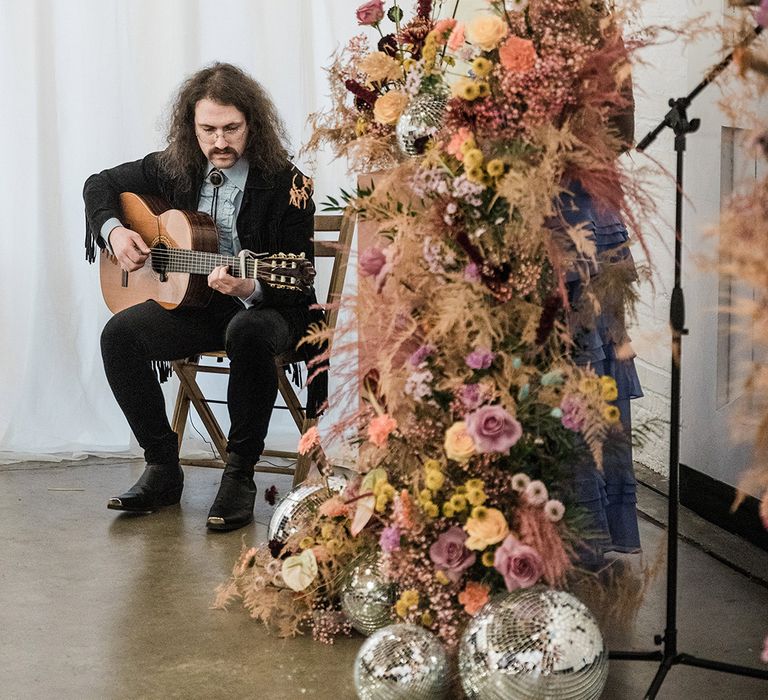 Guitar player plays during the wedding ceremony with flower columns and disco balls for altar decoration 