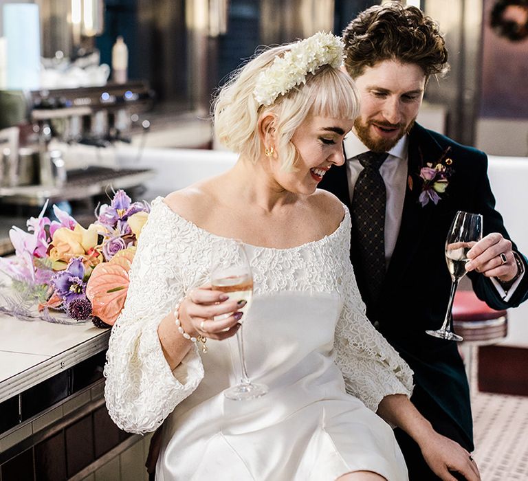 Bride and groom have a drink seated at a bar together with bouquet resting on the bar