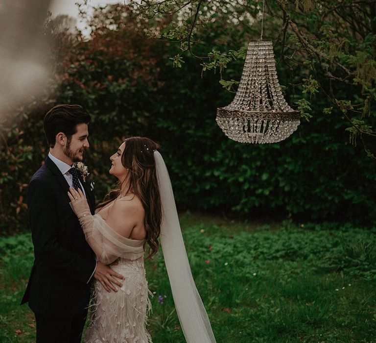 Bride and groom share a hug and look up at each other for their outside wedding at Millbridge Court with chandelier decor