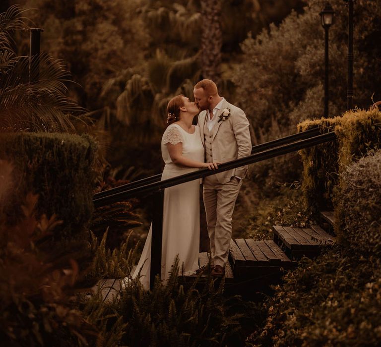 Bride & groom kiss on staircase outdoors at the Finca Villa Palma surrounded by trees and tropical florals 