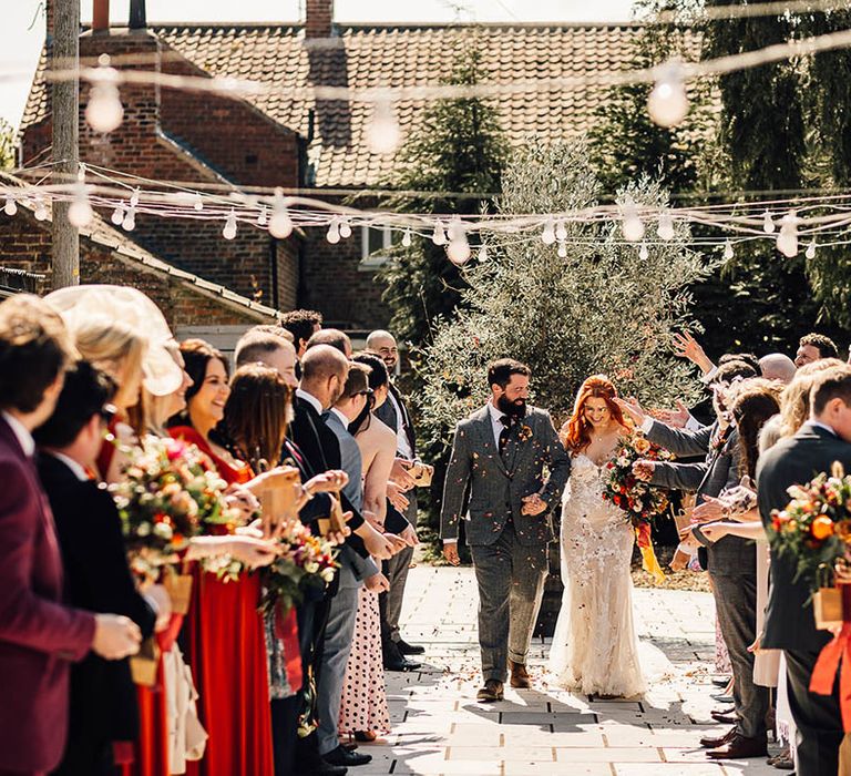 Bride in boho fitted lace dress and groom in a grey suit have a confetti moment 