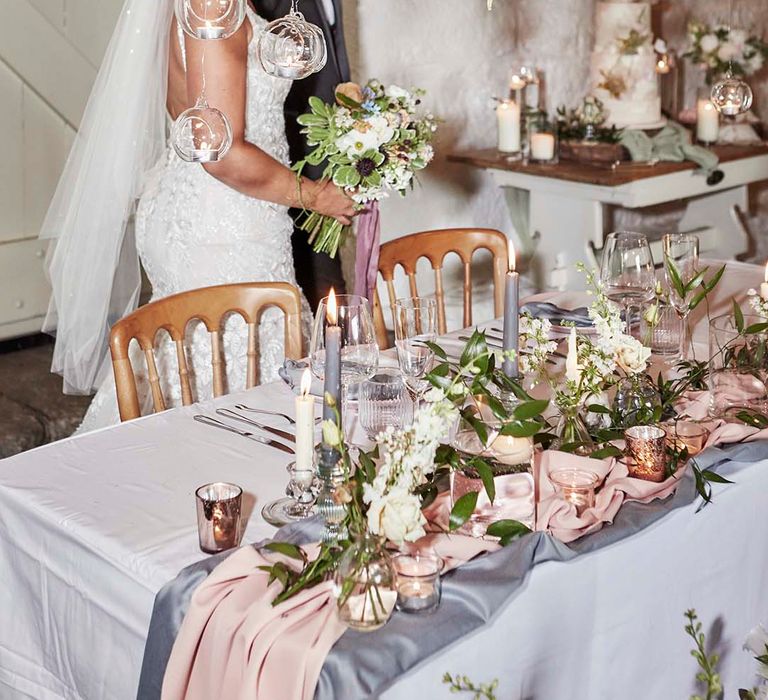 Sweetheart table with grey taper candles, votives, pink table runner, hanging votives and greenery floral arrangements 