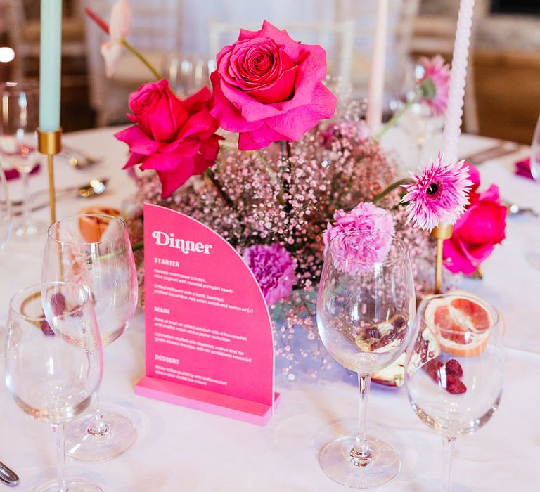 Bright pink floral centrepiece for modern tablescape surrounded by pastel candles 