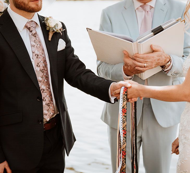 Bride wearing lace wedding dress during handfasting ceremony in front of the Thames river 