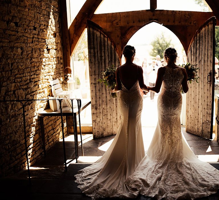 Brides in lace fitted wedding dresses with button back detail walk out of Cripps Barn to their wedding guests 