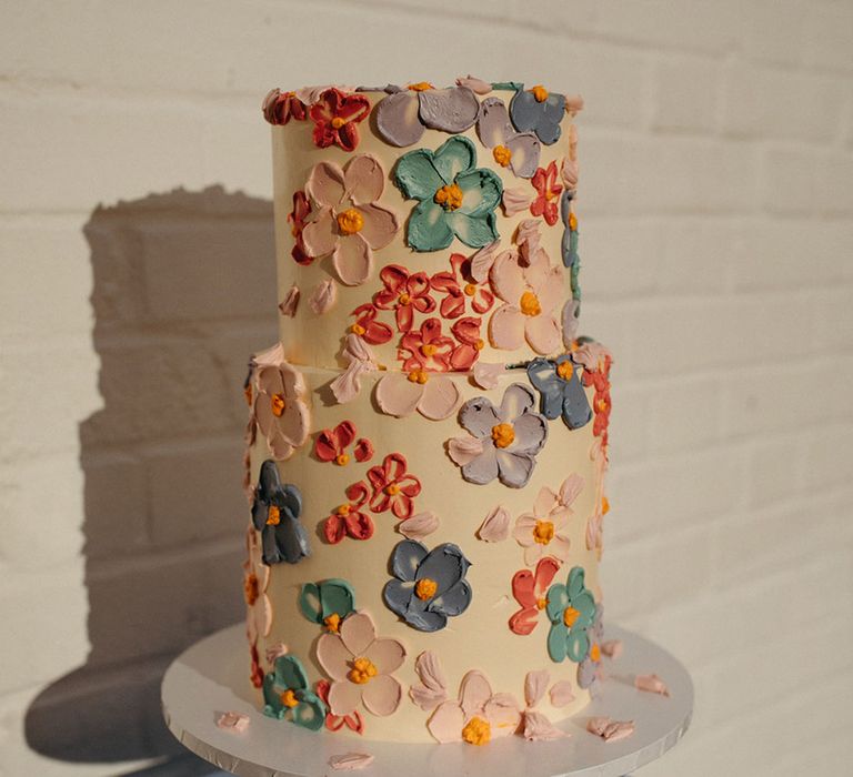 Two tier white iced wedding cake with colourful flowers iced on