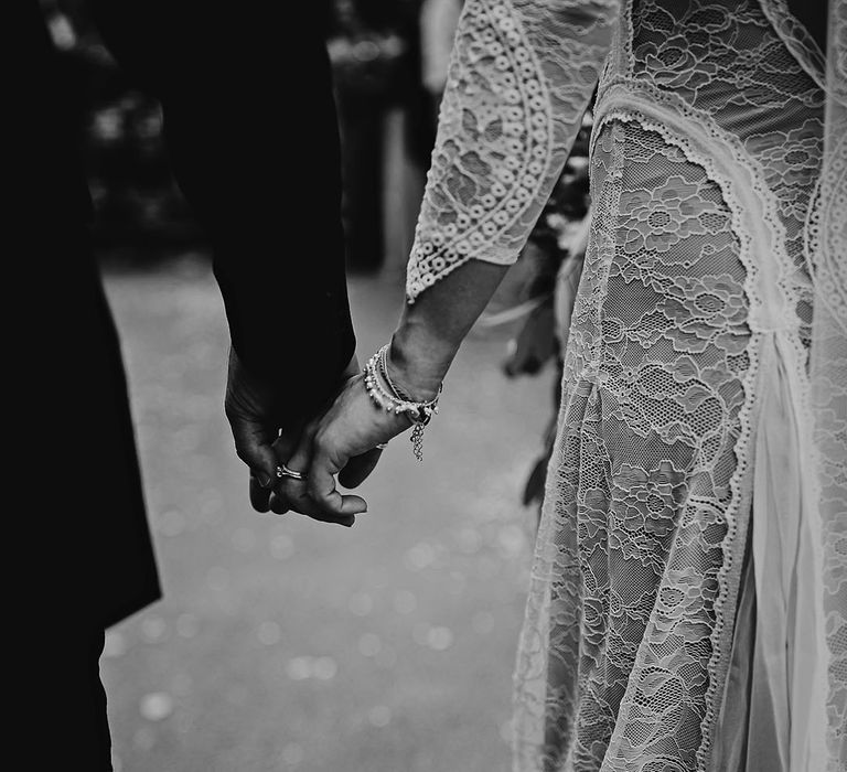 Bride in a boho lace wedding dress walks holding hands with the groom with the bride wearing bracelets and ring 